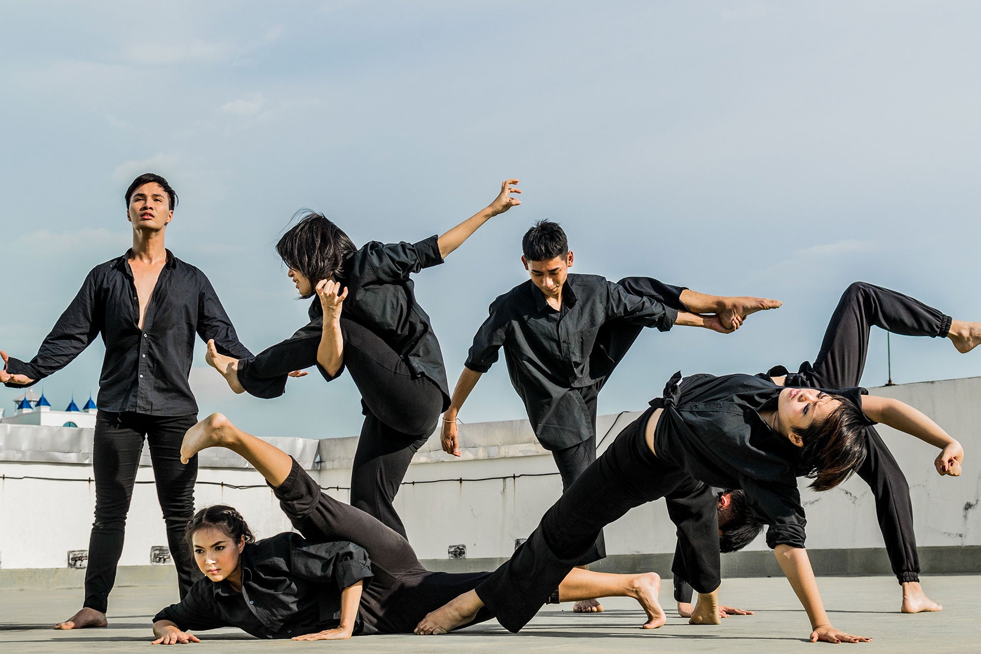 Stylized image with blue and purple gradient overlay of
	six dancers dressed in all black performing an interpretive dance.